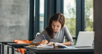 Woman writing in a notebook while sitting at her laptop